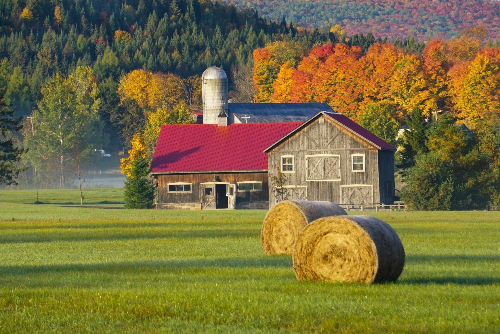Barn and round hay bales in a field during autumn