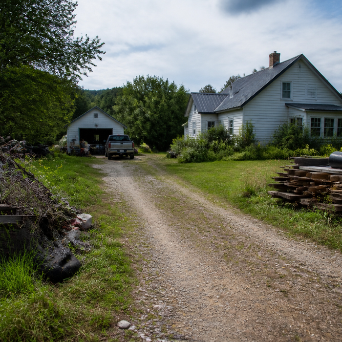 Gravel driveway leading through a wooden gate to a rural home