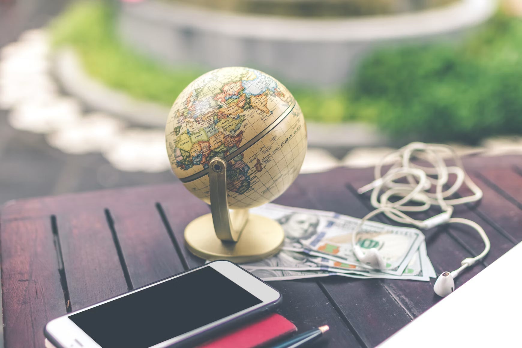 Globe, smartphone, currency, and travel items on an outdoor table