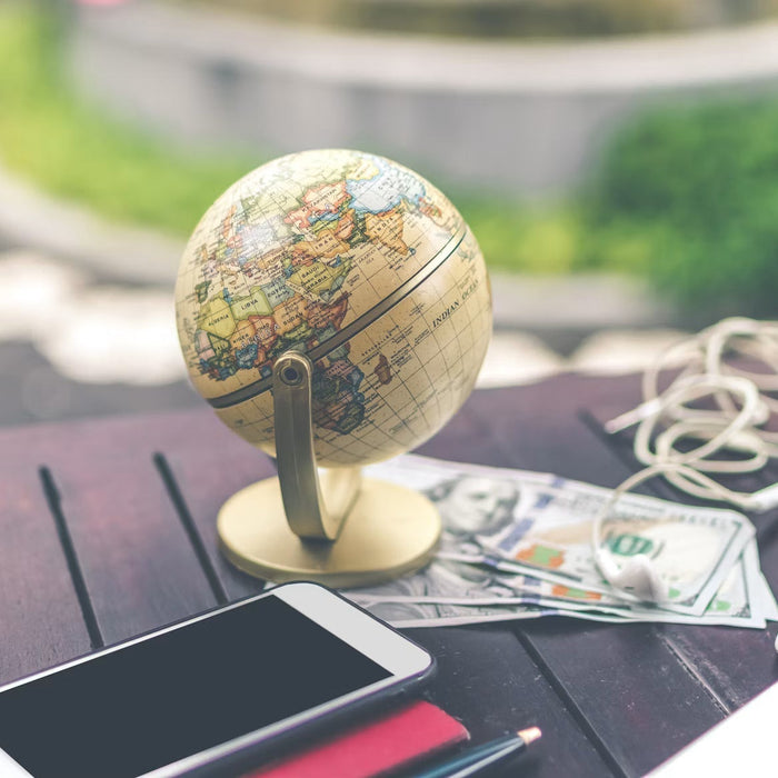Globe, smartphone, currency, and travel items on an outdoor table