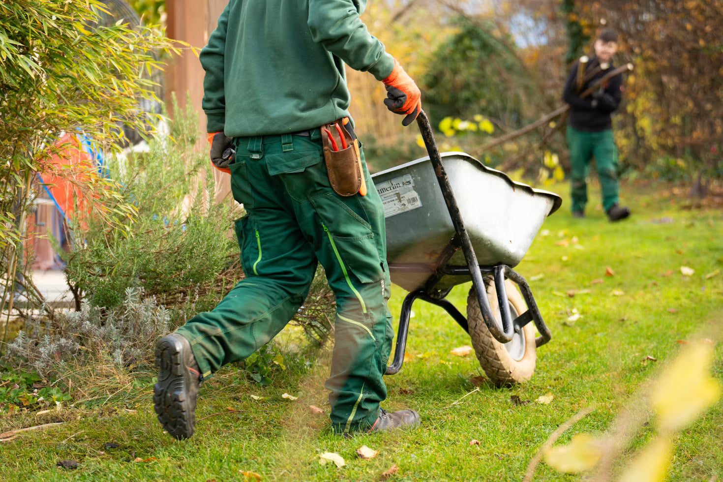 Landscaping crew carrying tools and a wheelbarrow beside a home