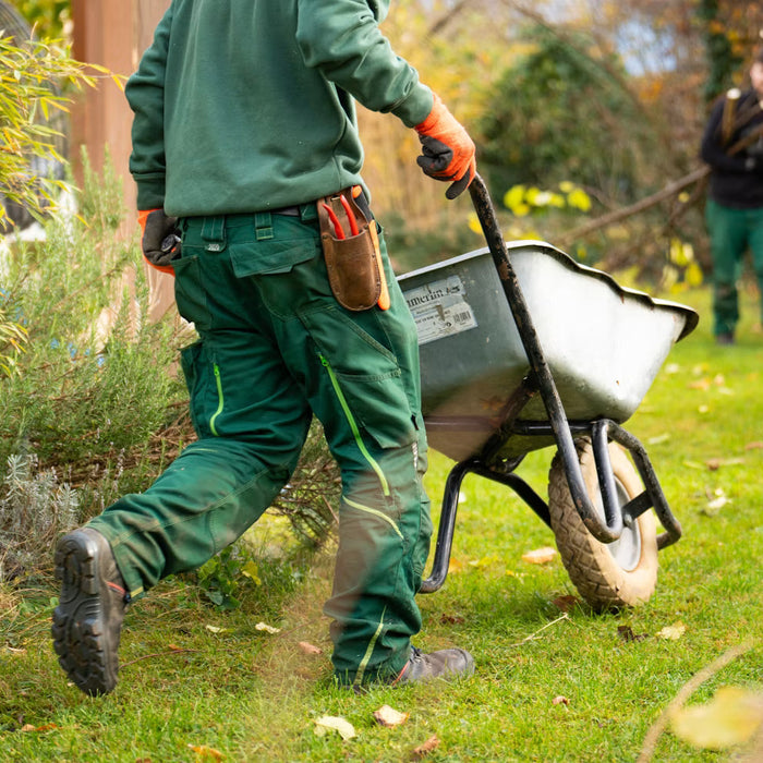 Landscaping crew carrying tools and a wheelbarrow beside a home