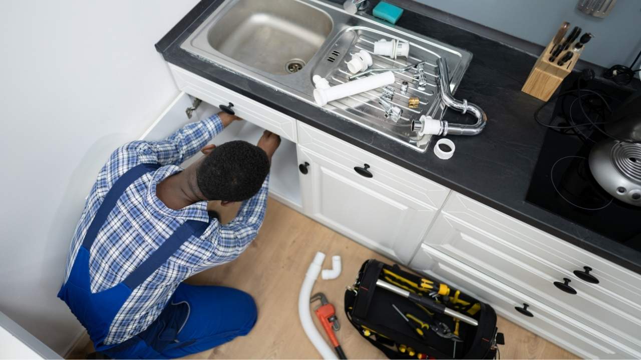 Plumber repairing pipes beneath a kitchen sink