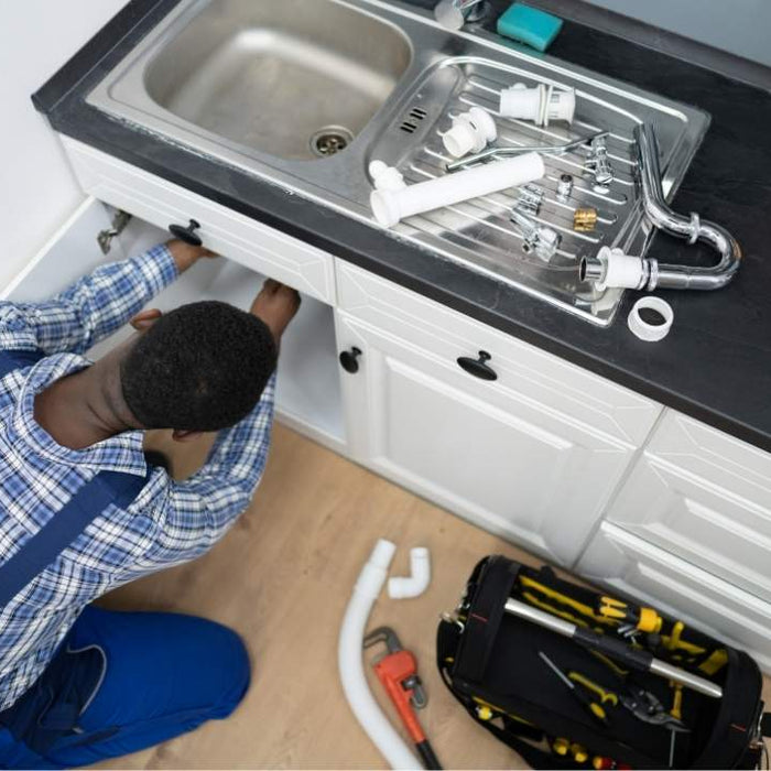 Plumber repairing pipes beneath a kitchen sink