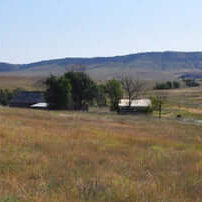Open rural homestead landscape with fields, hills, and a farmhouse