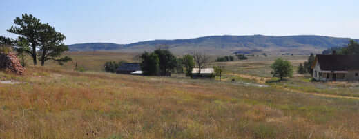 Open rural homestead landscape with fields, hills, and a farmhouse