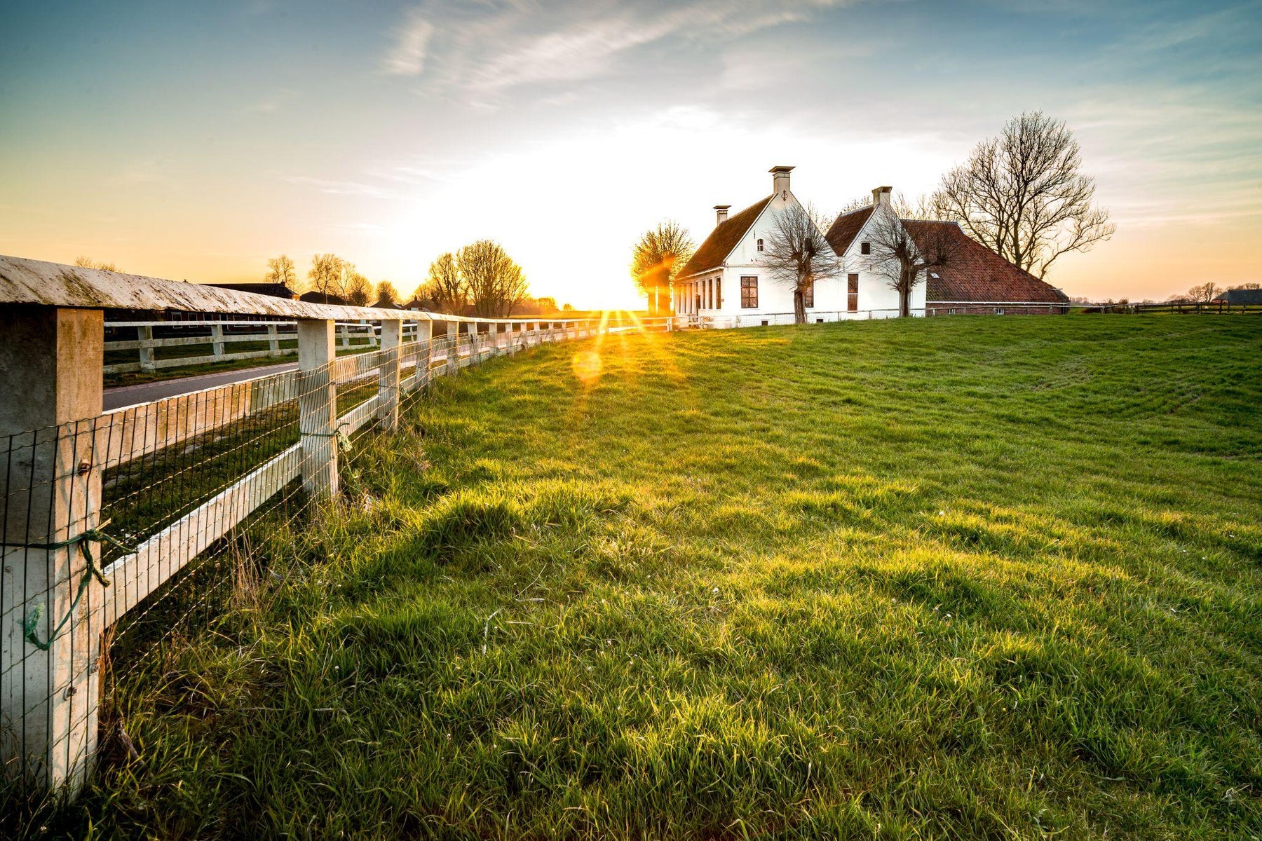 Fence leading toward a rural house across green grass