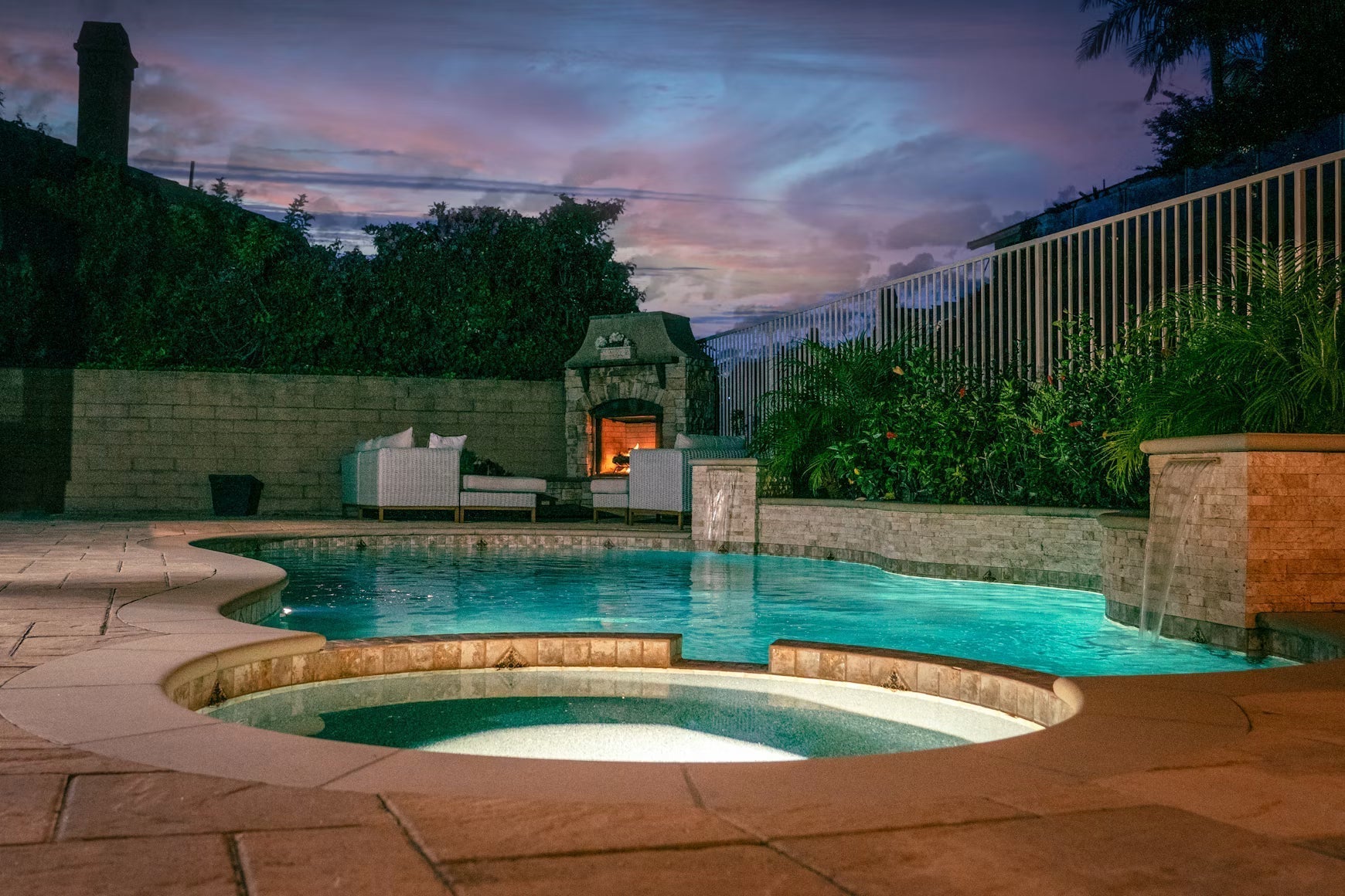 Backyard pool and spa beside an outdoor fireplace at sunset