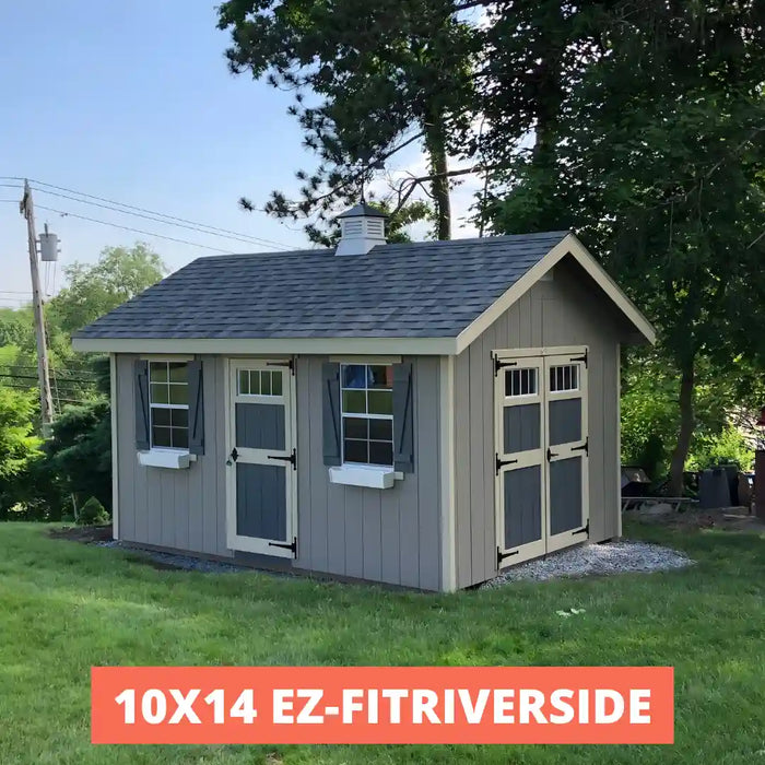 EZ-Fit Riverside Storage Shed Kit with a gray roof and beige walls in a grassy area with trees.