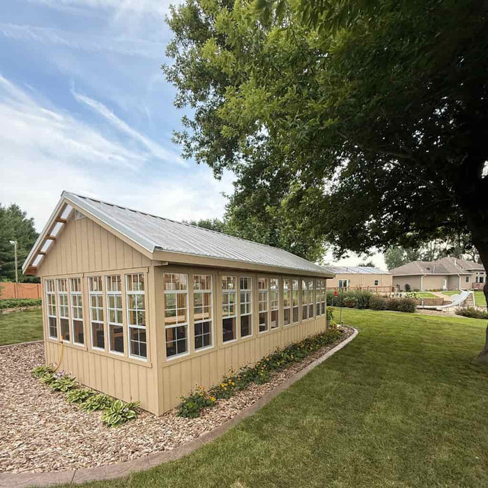 Ez fit 12x24 greenhouse kit with glass panels on a grassy area with trees and houses in the background