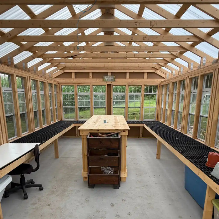 Ez fit 12x24 greenhouse interior with wooden benches and tables, large windows, and a clear sky outside.