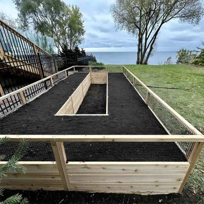 Outdoor Living Today 8x16 cedar raised garden bed with soil in a grassy area near a body of water.
