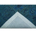 Underside corner of the blue wool rug showing the backing and bound edge