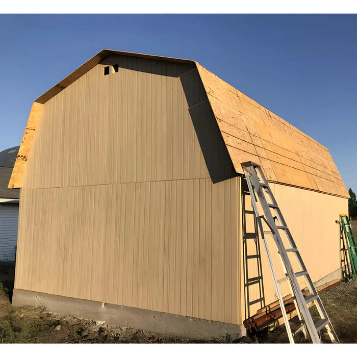 Little cottage co gambrel large barn under construction with wooden siding and a ladder against a clear blue sky.