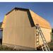 Little cottage co gambrel large barn under construction with wooden siding and a ladder against a clear blue sky.