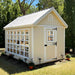 Colonial gable greenhouse with white trim in a garden setting