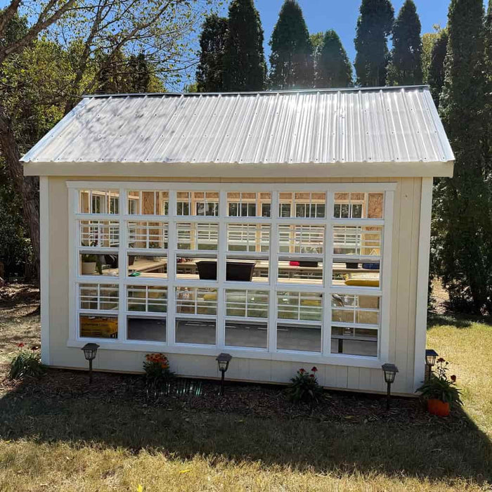 White colonial gable greenhouse with large windows in a garden setting