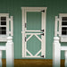 Little Cottage Co Craftsman Playhouse Kit white wooden dutch door with black hardware on a green paneled wall