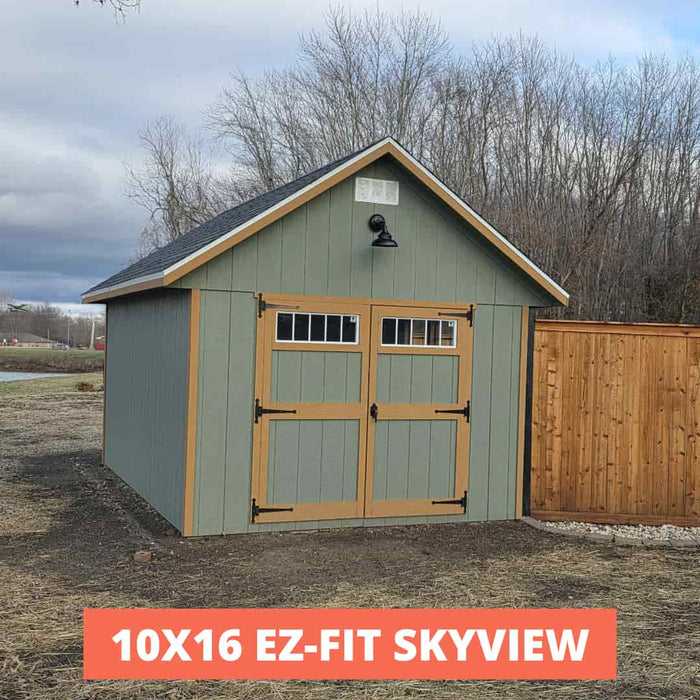 Green storage shed with wooden doors in a rural setting, labeled '10x16 EZ-FIT SKYVIEW'.