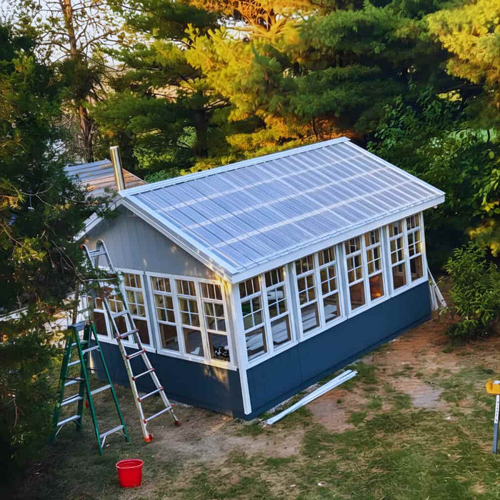 EZ-Fit Greenhouse Kit with solar panels on the roof surrounded by trees