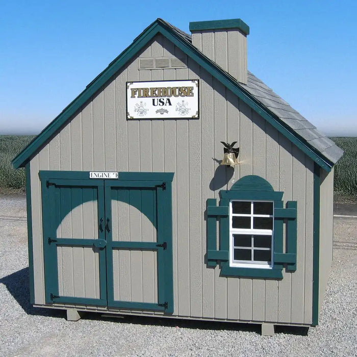 Small playhouse resembling a firehouse with green trim and a sign on a clear day.
