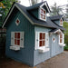Children's palmako marie 9x6 playhouse with a blue exterior and white trim in a natural setting