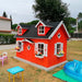 Red palmako marie 9x6 wood playhouse kit with black roof in a backyard setting