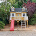 Wooden palmako marie 9x6 playhouse with a red slide and white ladder in a garden setting