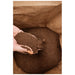 Hand holding loose OverEZ Coffee Ground Bedding inside an opened package.