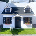 Small white palmako marie 9x6 playhouse with black shutters and a blue door, featuring two small windows on the roof.