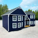 Navy blue Little Cottage Co. Sara's Victorian playhouse with white trim on a gravel surface with trees in the background
