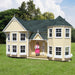 Little Cottage Co. Sara's Victorian Children's playhouse with a girl standing inside, surrounded by trees and grass.