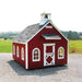 Little Cottage Co Stratford Schoolhouse playhouse kit with white trim on a gravel surface with a grassy field and trees in the background.