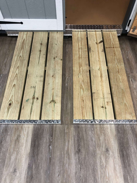 Wooden ramp with metal diamond plate door threshold, placed on a brown wooden floor.